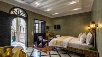 Una habitación con una cama, una silla, una mesita, una lámpara decorativa y un ventanal amplio.