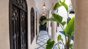 Un pasillo con puertas negras ornamentadas, suelo de baldosas y una lámpara colgante.