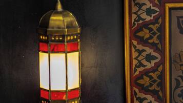 A wall-mounted lantern with a red and gold design, a framed artwork with a floral pattern, and a white pillow on a dark surface.