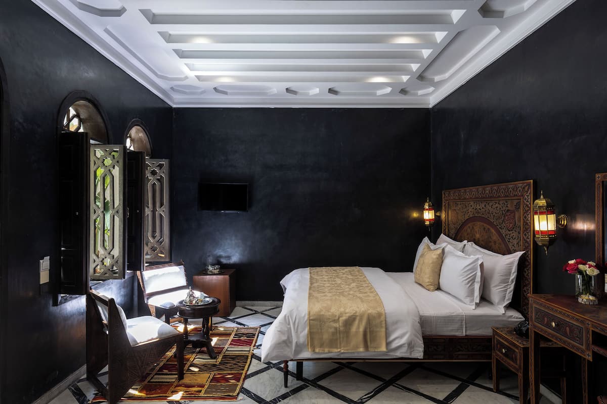 A bedroom with a bed, bedside table, chair, and a decorative wall panel.