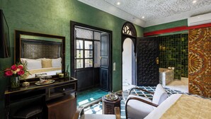 Habitación de hotel con cama, escritorio, silla, mesita con bandeja y un jarrón decorativo con flores.