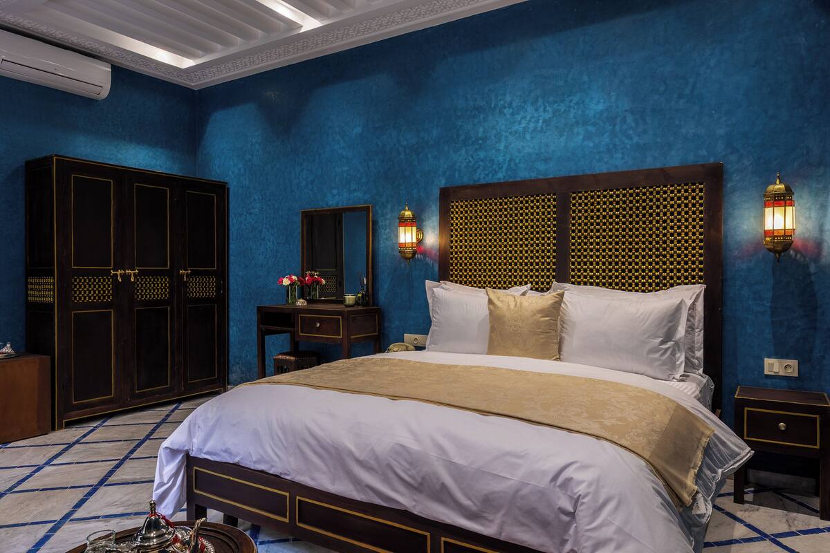 A bedroom with a large bed, a wardrobe, a nightstand, and two wall-mounted lamps.