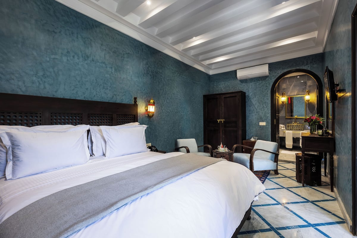 A hotel room with a large bed, a desk, a chair, and a mirror.