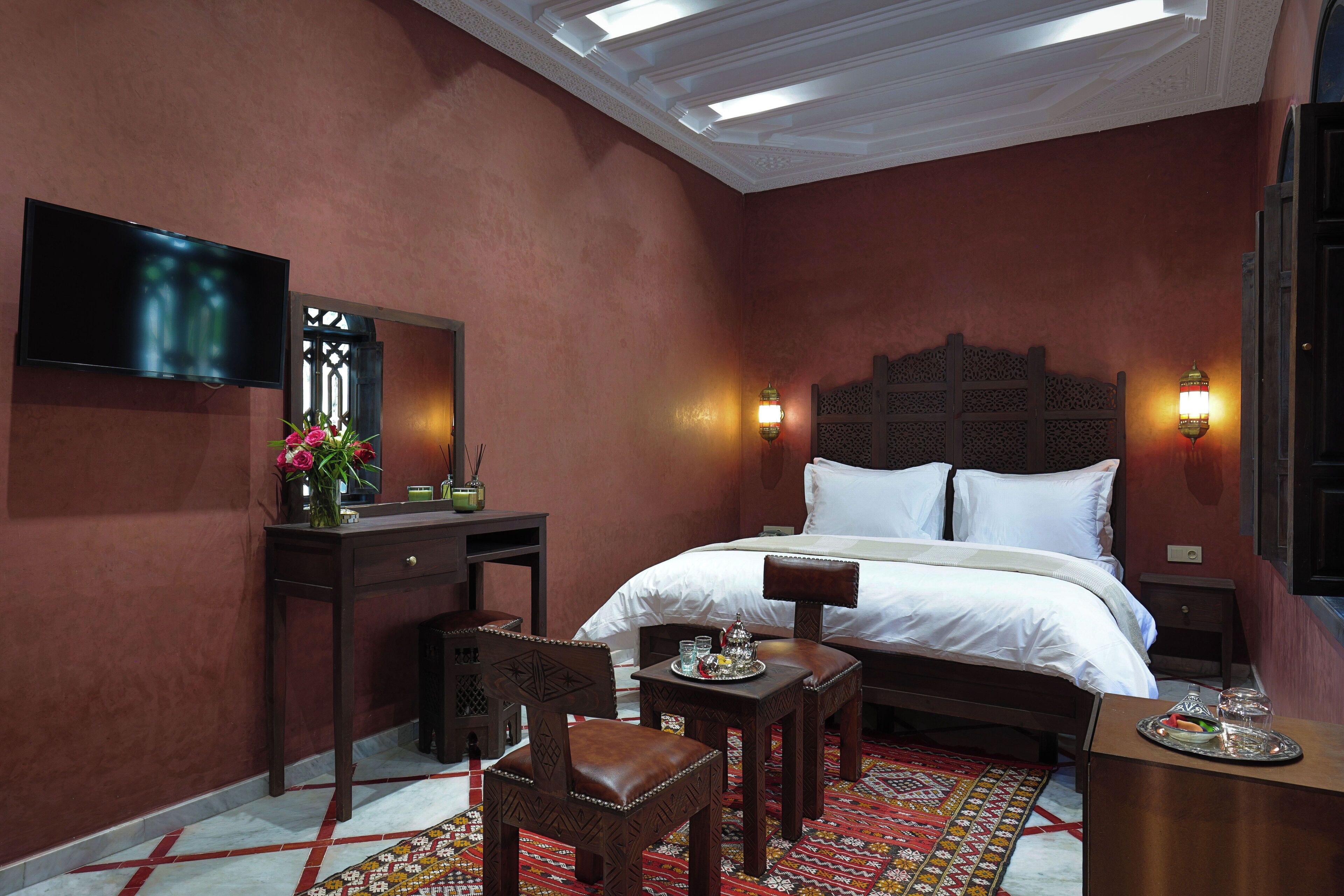 Habitación de hotel con cama, escritorio, silla, televisor y una lámpara decorativa en la pared.