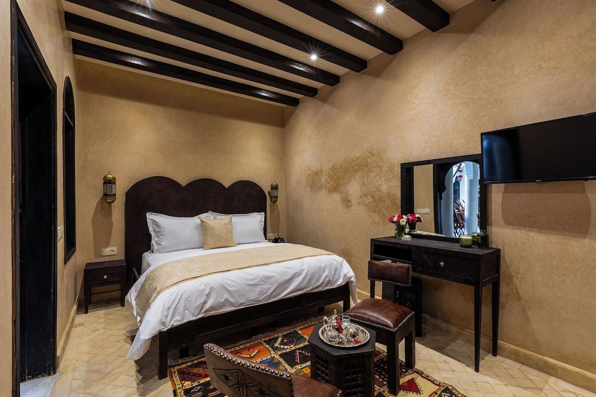 A bedroom with a large bed, a small bedside table, a chair, a dresser, and a television.