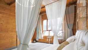 Dormitorio de una cabaña de madera con una cama, cortinas blancas y una ventana.