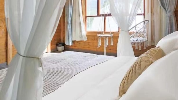 Un dormitorio con cama con dosel, paredes de madera y una ventana con cortinas.