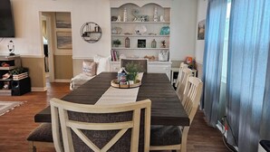 Un comedor con una mesa larga, sillas, un estante decorativo con varios objetos y un reloj en la pared.