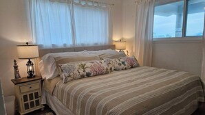 Un dormitorio con una cama grande, dos mesitas de noche con lámparas, una mesita auxiliar y una ventana con cortinas.
