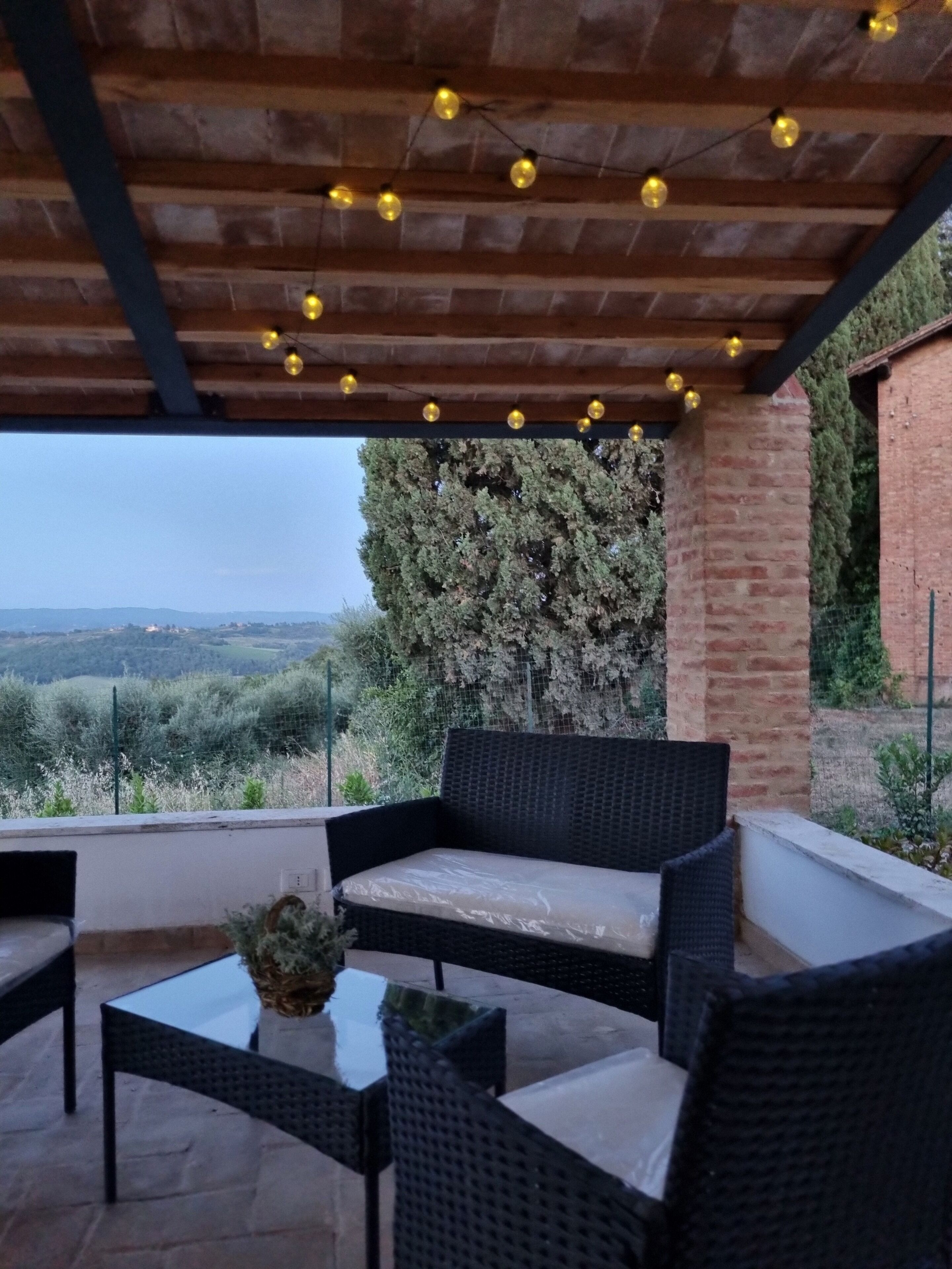 An outdoor patio with wicker furniture, a glass table, and string lights.