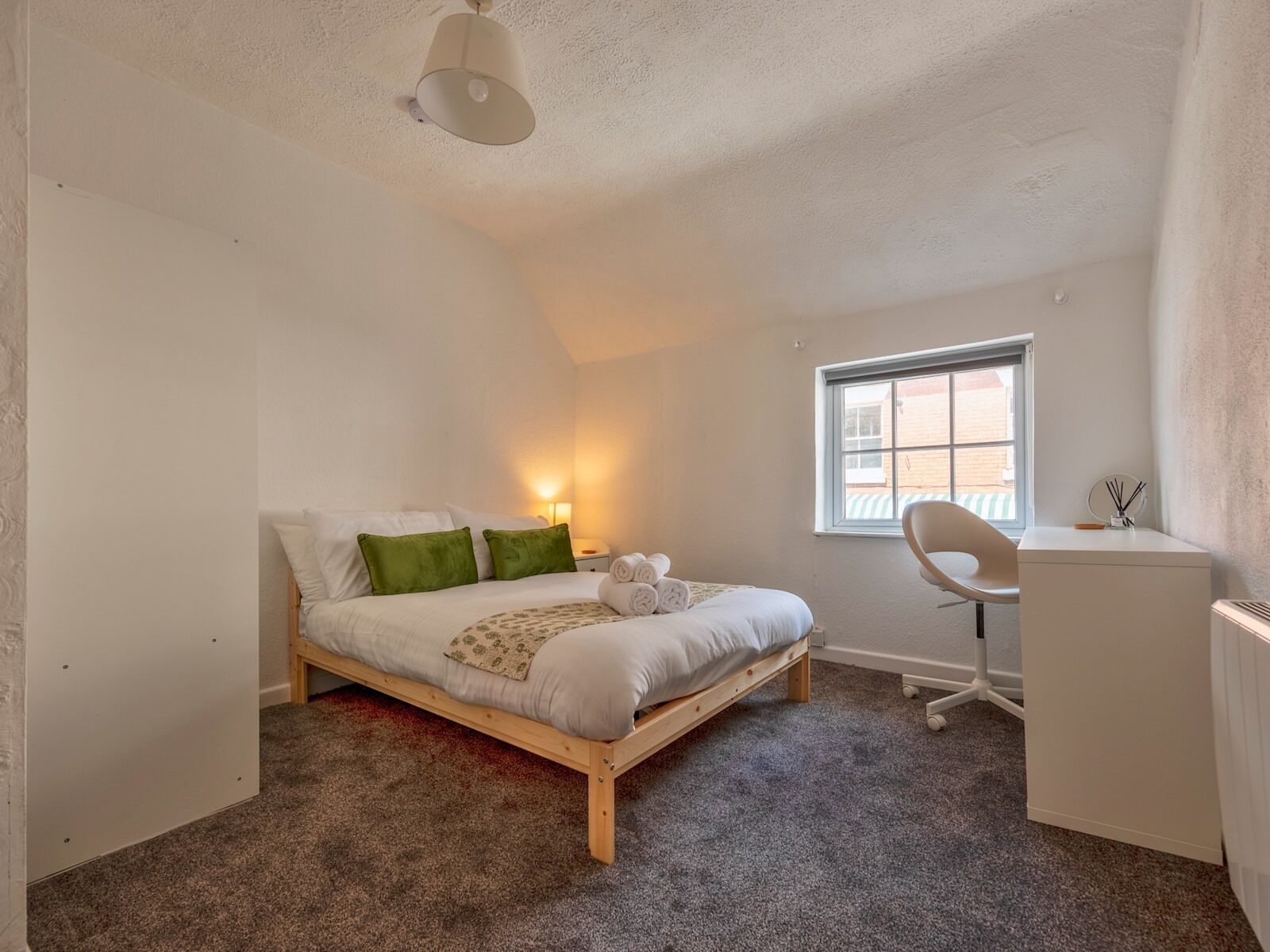 Ein Schlafzimmer mit einem Bett, einem Schreibtisch, einem Stuhl, einem Fenster und einer Lampe.