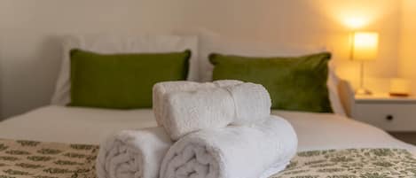 A neatly made bed with rolled white towels, green pillows, and a patterned bedspread.