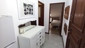 Un couloir étroit avec un réfrigérateur blanc, un meuble blanc doté de tiroirs et une porte en bois.