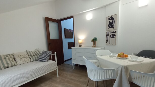 Un salon moderne avec un canapé, une table à manger et des chaises. On y trouve une porte en bois, un petit meuble et des œuvres d’art murales.