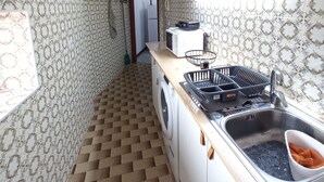 Une cuisine compacte avec un papier peint à motifs, un lave-linge, un four à micro-ondes et un évier équipé d’un égouttoir.