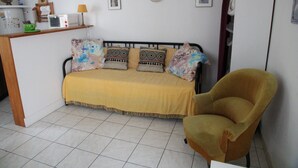 A small, cozy room with a bed, a chair, a shelf with a microwave, and a small table. - A 10 Minutes des Thermes et des Remontées, Appartement Classé 2 Étoiles (Cauterets)