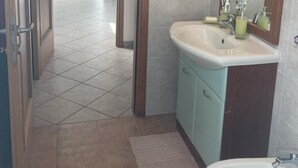 Une salle de bain avec un lavabo, un miroir et des toilettes. Une porte donne accès à une autre pièce.