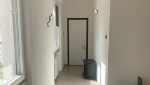 Un couloir étroit au sol carrelé, avec une porte au fond et une poubelle au milieu.