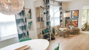 Ein modernes Wohnzimmer mit einem weißen Tisch, grünen Stühlen, einem Korbssessel und einem Bücherregal.