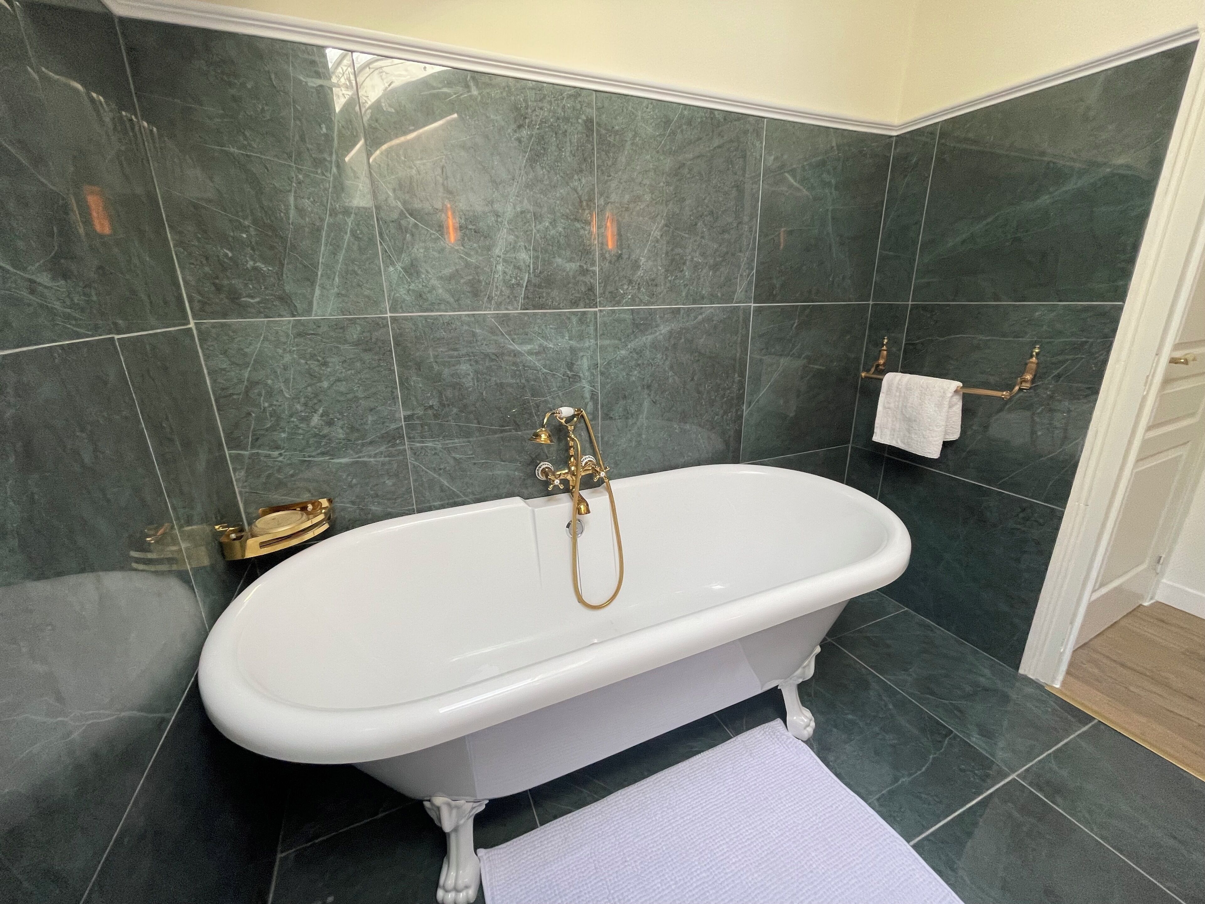 Une salle de bain avec une baignoire sur pieds, des carreaux de marbre foncé et un porte-serviettes blanc.
