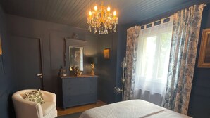 Un dormitorio con una cama grande, un aparador, una silla, una araña de cristal y una ventana con cortinas.