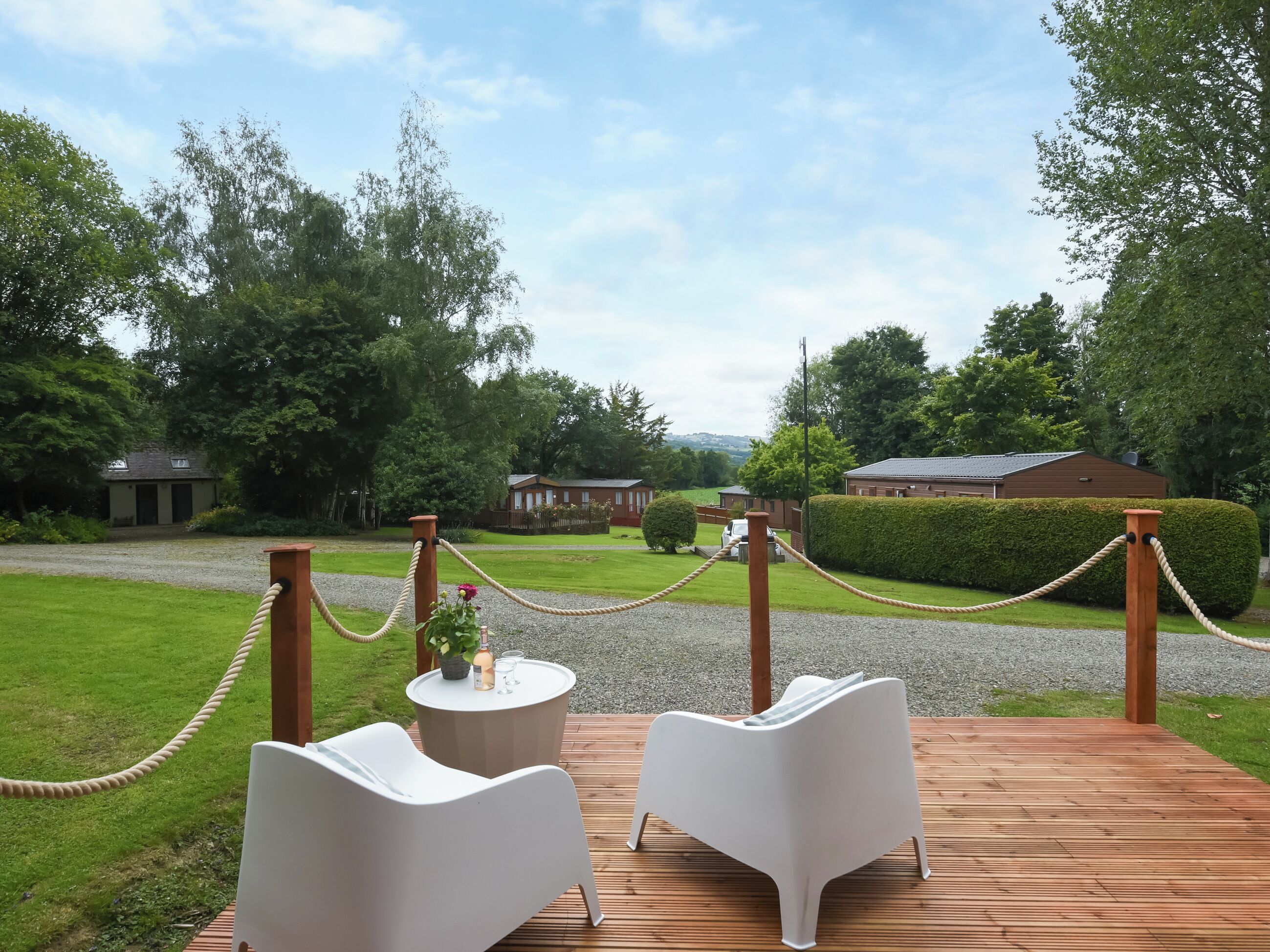 A wooden deck with two white chairs and a round table with a bottle and glasses.