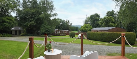 A wooden deck with two white chairs and a round table with a bottle and glasses.