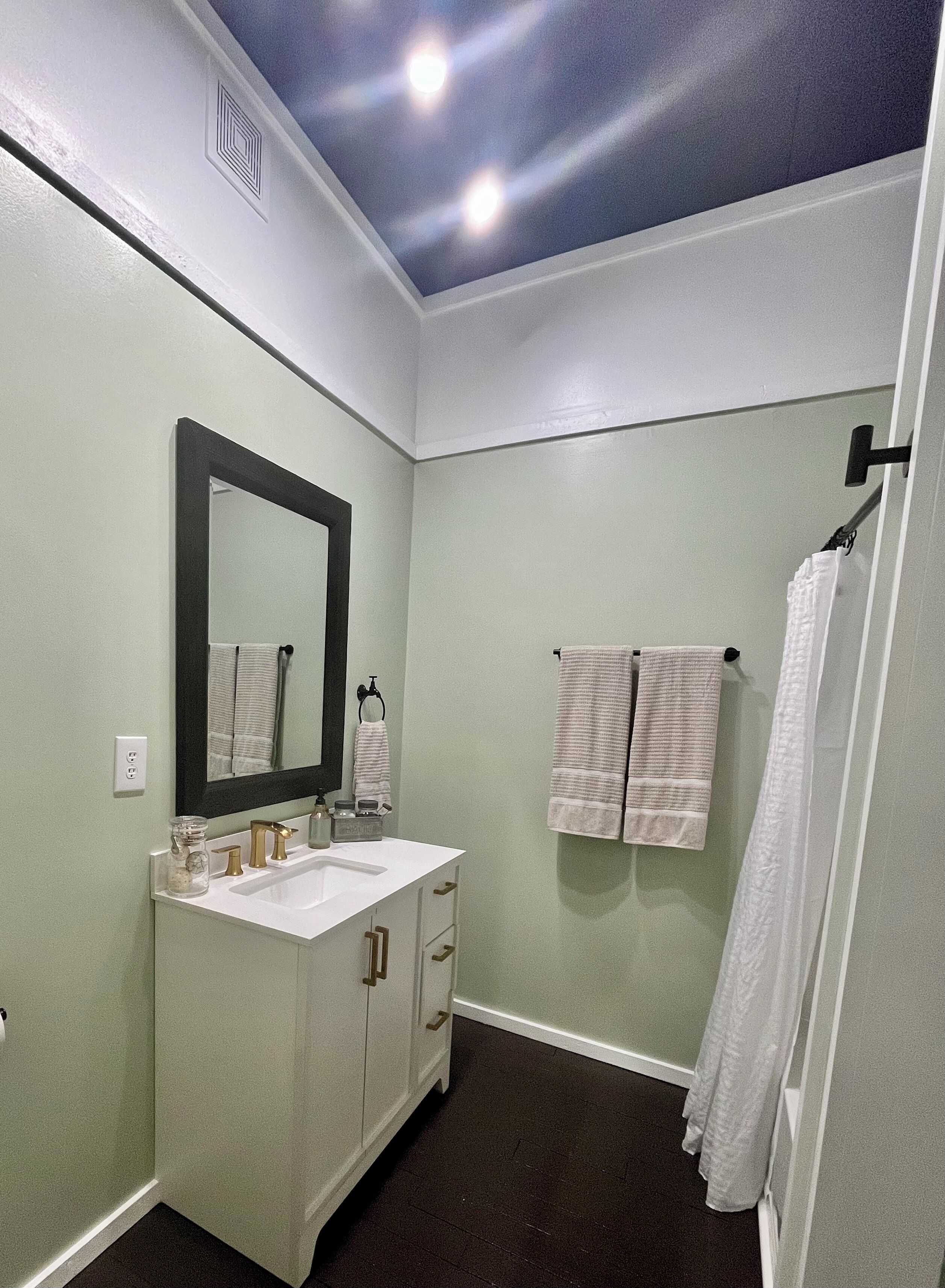 Une salle de bain avec un lavabo blanc, un grand miroir et deux serviettes suspendues à des crochets.