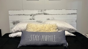 A bed with a gray pillow that reads "STAY AWAY." Two framed pictures are hung on the wall above the bed. - Fun 2 BdRm Apt in the Bourbon Capital with Pool Table, PAC-Man & More! (Bardstown)