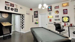 A pool table in a room with a ceiling fan, a dartboard, and various wall decorations including beer and liquor brand signs. - Fun 2 BdRm Apt in the Bourbon Capital with Pool Table, PAC-Man & More! (Bardstown)