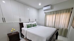 A bedroom with a bed, a nightstand, a wardrobe, and a window with curtains. - The Swallow Nest 1 (Gros Islet)