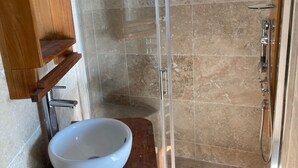 Een badkamer met een douchecabine van glas, een witte wastafel en een houten opbergmeubel.