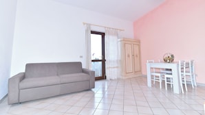 A living room with a sofa, a dining table with chairs, a cabinet, and a door with a view to the outside. - La Costa Mare (Arzachena)