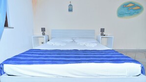 A neatly made bed with a blue and white striped blanket, two bedside tables with lamps, and a wall decoration of fish. - La Costa Mare (Arzachena)
