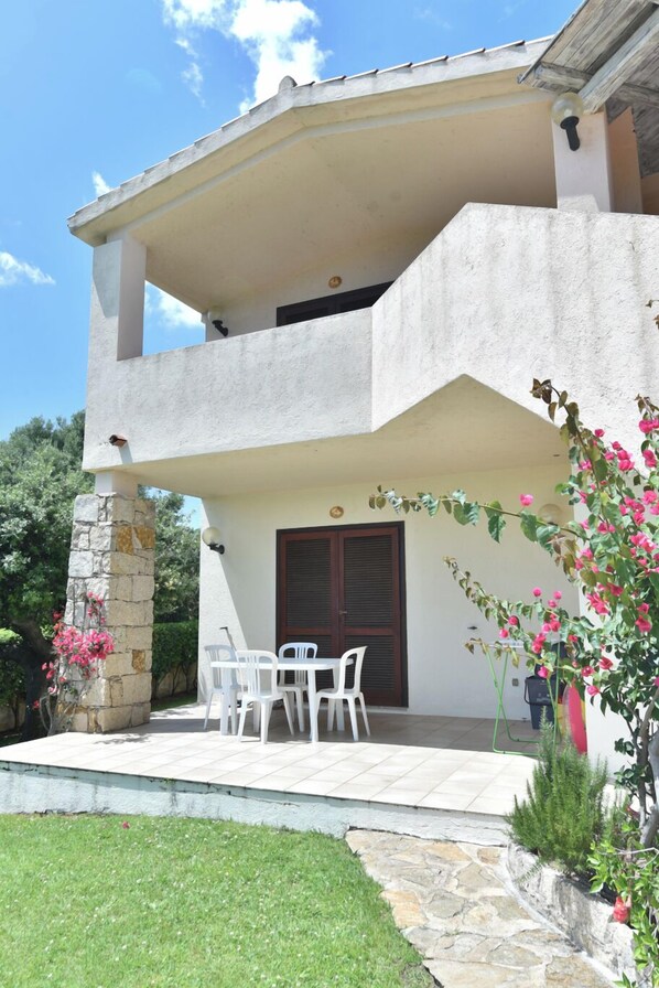 A two-story building with a balcony, a stone pillar, and a small patio area with a table and chairs.