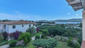 A white villa with a tiled roof overlooking a lush garden and a body of water. - La Costa Mare (Arzachena)