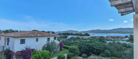 A white villa with a tiled roof overlooking a lush garden and a body of water.
