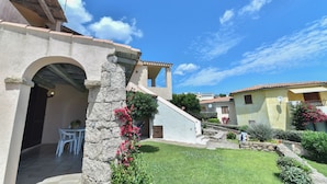 A traditional Mediterranean-style building with a stone archway, a small patio with white chairs, and a well-maintained garden. - La Costa Mare (Arzachena)