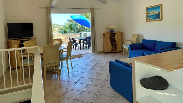A living room with a television, a blue sofa, and a dining area with chairs and a table.