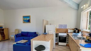 A compact living space with a kitchenette, a blue sofa, a small dining table, and a window with a view.