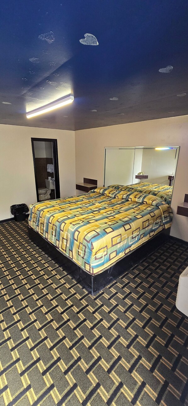 A hotel room with a large bed, a mirror, and a patterned carpet.