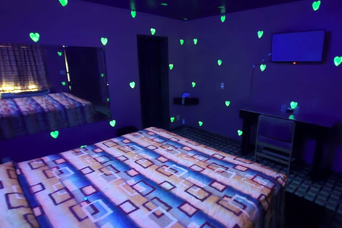 Una habitación con una colcha estampada, un televisor de pantalla plana en la pared y un escritorio con una silla.