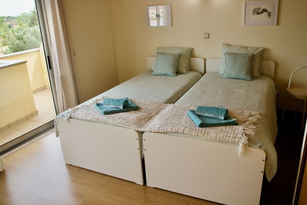 A room with two beds, a small table, and a window with a view of greenery.