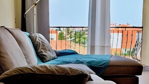 Ein Wohnzimmer mit einer Couch, einer Lampe und Blick auf einen Balkon mit Geländer.