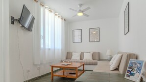 Ett vardagsrum med en platt-TV som är monterad på väggen, en takfläkt, en soffa, ett soffbord och en inramad tavla av Picasso.