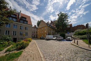 Una calle adoquinada bordeada por edificios de varios pisos, coches estacionados y una señal de estacionamiento.