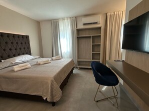 Une chambre d’hôtel comprenant un lit, un bureau, une chaise, une télévision et une armoire.