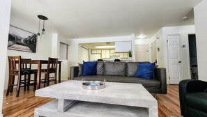 Un salon avec un canapé gris, une table basse et un coin repas avec des chaises en bois.