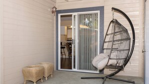 A covered patio with a hanging chair, two wicker ottomans, and a sliding glass door leading to an interior space. - Adventurers Base Camp! (Boise)