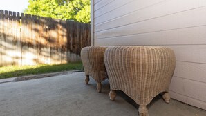 Two wicker outdoor tables with curved legs, positioned on a concrete patio next to a white wooden wall. - Adventurers Base Camp! (Boise)